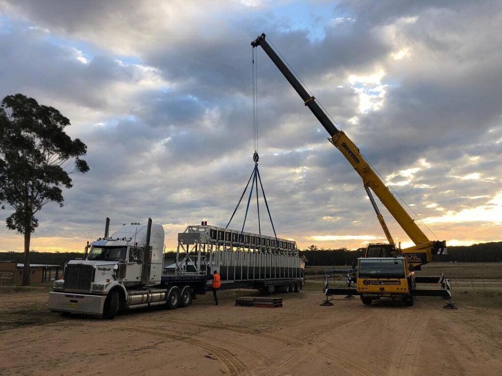 Mobile crane lifting large metal structure from truck at South East Civil & Crane worksite.