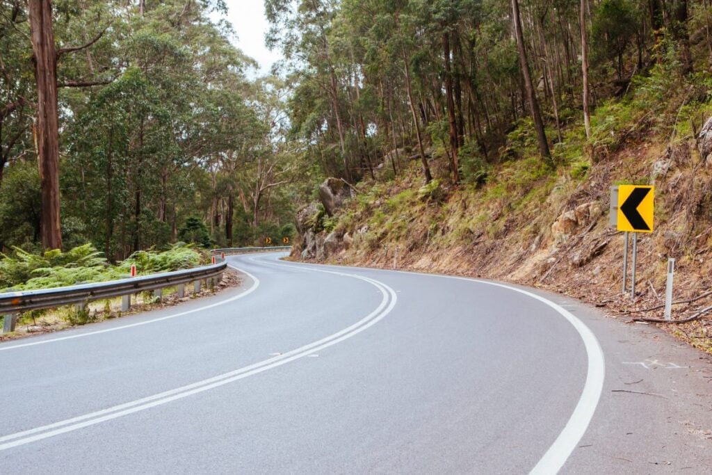 Curved sealed road with guardrails and arrow sign through forest area by South East Civil & Crane.