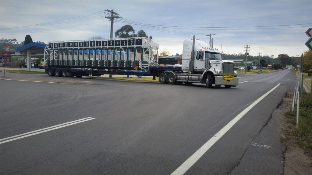 A large white semi-truck transporting a specialized piece of equipment—a mobile horse racing starting gate.