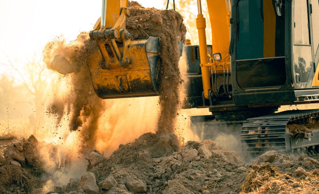 A yellow excavator actively digging and moving dirt.