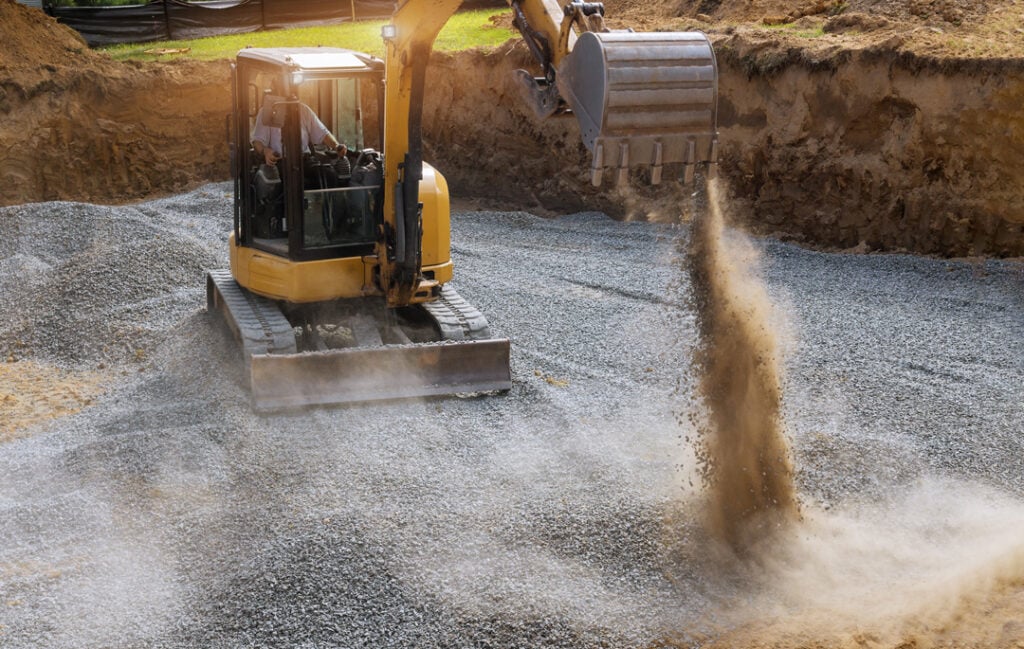 Excavator bucket moving gravel stones for foundation building working on a construction site