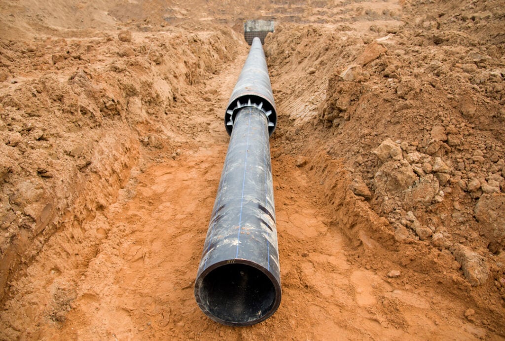 A trench, looking down the length of a large, newly laid pipe that is part of a utility or drainage installation.