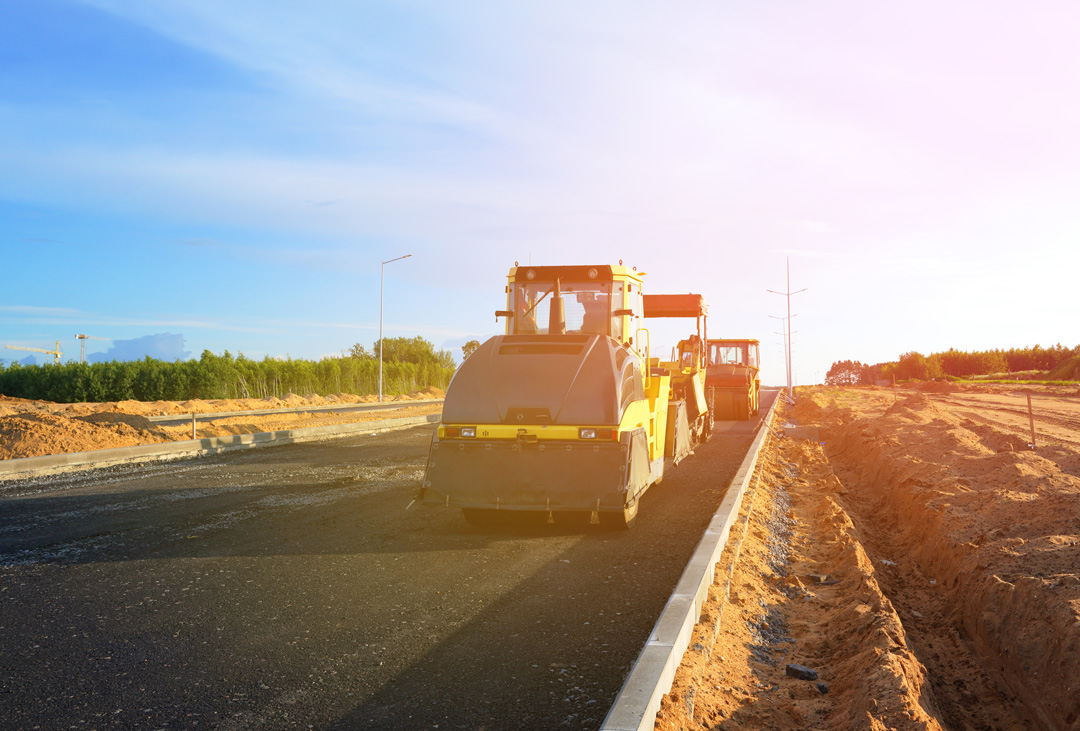 Road roller and paver laying asphalt on new roadway by South East Civil & Crane.